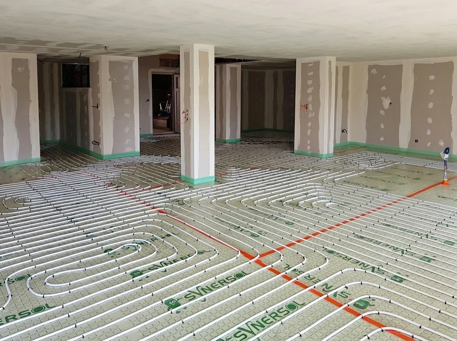 Gros plan ou vue d'ensemble d'un sol r&eacute;sidentiel avec syst&egrave;me de plancher chauffant visible lors de son installation ou en fonctionnement - montrant les tubes de circulation d'eau chaude int&eacute;gr&eacute;s dans la dalle ou le rev&ecirc;tement de sol dans un int&eacute;rieur domestique moderne et confortable.