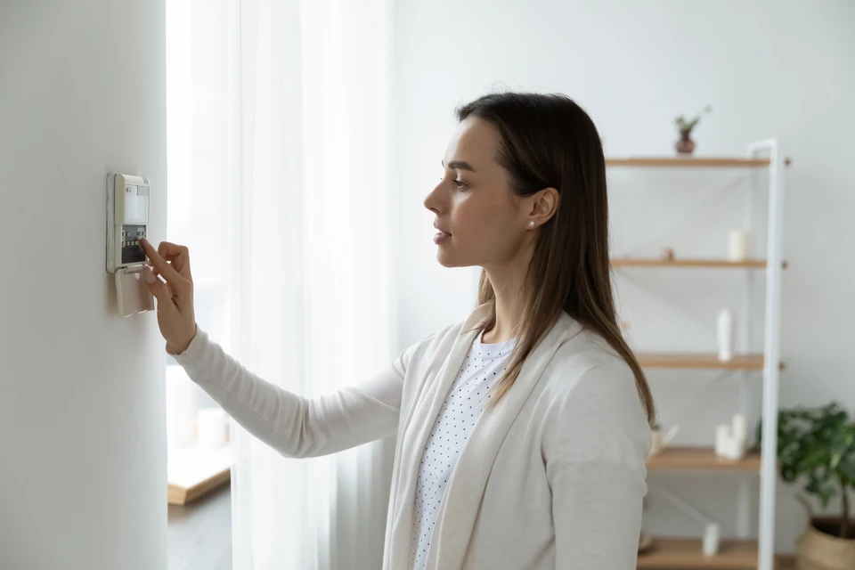 Femme en cardigan blanc utilisant un thermostat numérique mural dans un intérieur moderne