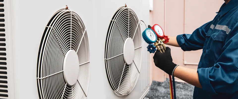 Un technicien en climatisation travaille à l'extérieur sur une unité de climatisation murale
