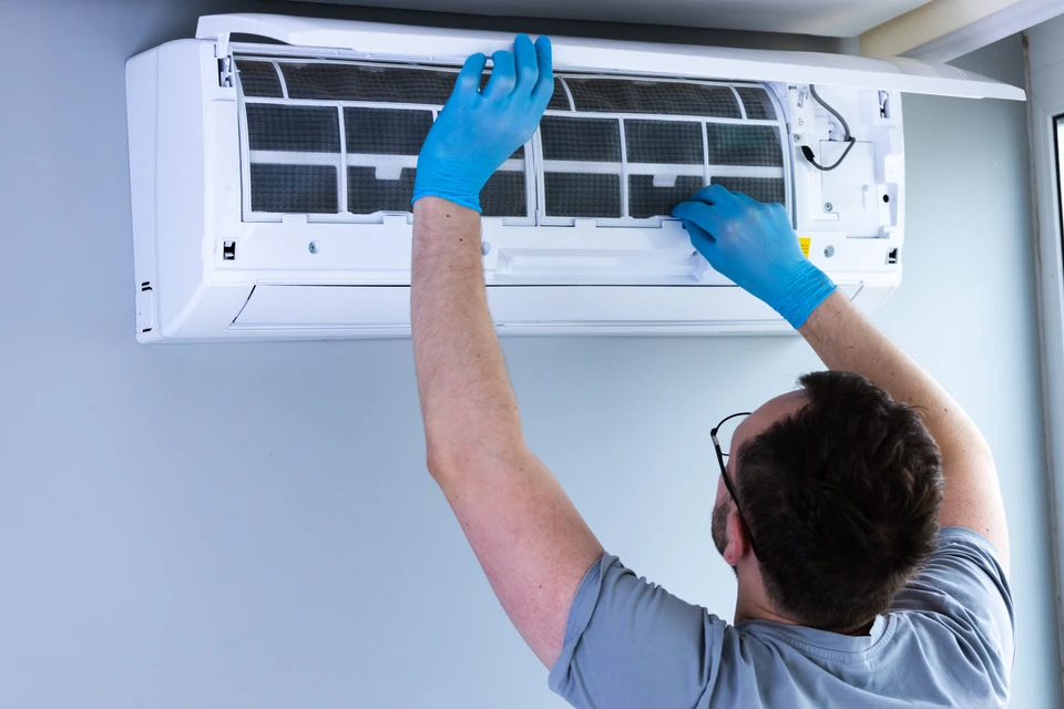Un technicien en climatisation travaille à l'extérieur sur une unité de climatisation murale