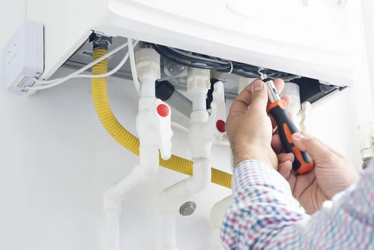 Technicien chauffagiste en uniforme professionnel effectuant un d&eacute;pannage urgent sur une chaudi&egrave;re murale domestique, en train de v&eacute;rifier les connexions hydrauliques ou le panneau de contr&ocirc;le avec un multim&egrave;tre ou un appareil de diagnostic, dans un int&eacute;rieur r&eacute;sidentiel r&eacute;aliste montrant la relation de confiance avec le client ou son intervention focalis&eacute;e sur l'&eacute;quipement. La sc&egrave;ne doit mettre l'accent sur l'expertise technique et la professionnalit&eacute; du d&eacute;pannage d'urgence.